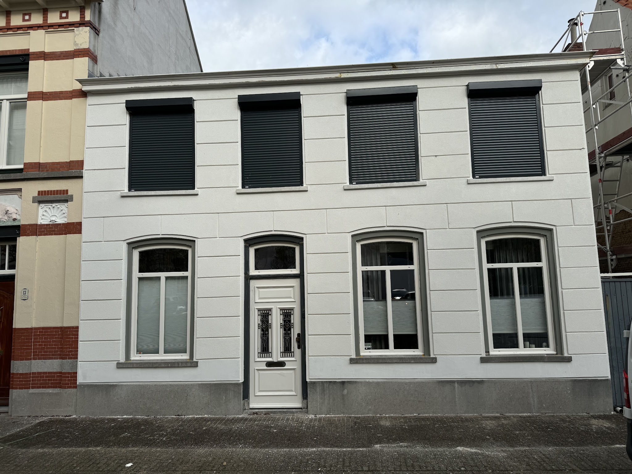 Voorgevel van een rijtjeswoning, strak wit gestuct met blokverdeling en grijze kozijnranden