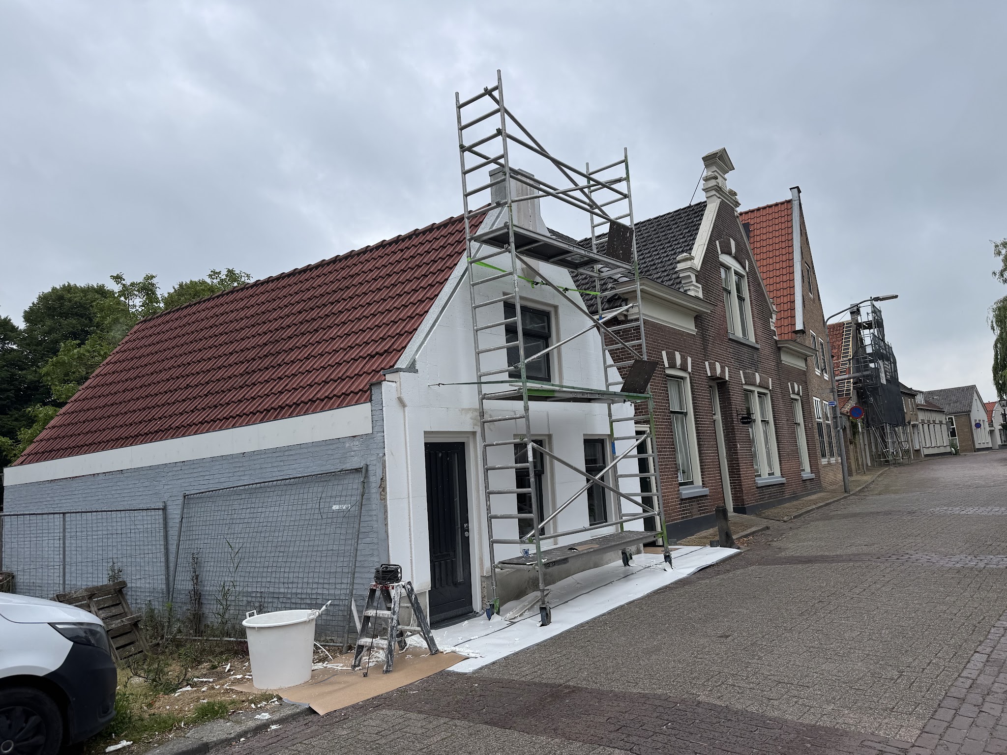 Woning aan een klinkerstraat met verse witte stuclaag en een rolsteiger