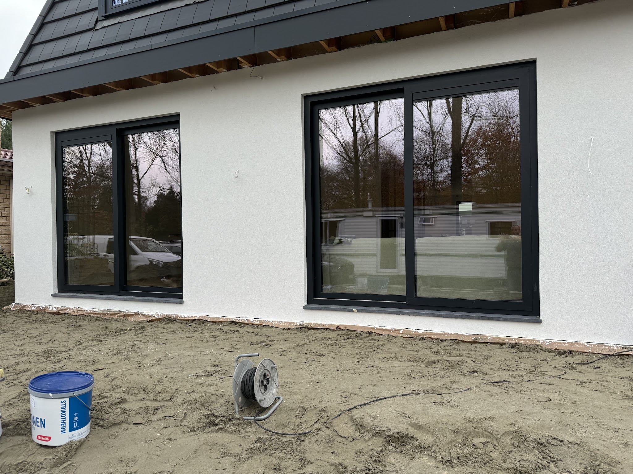 Achtergevel van een nieuwbouwwoning, wit gestuct met grote zwarte kozijnen