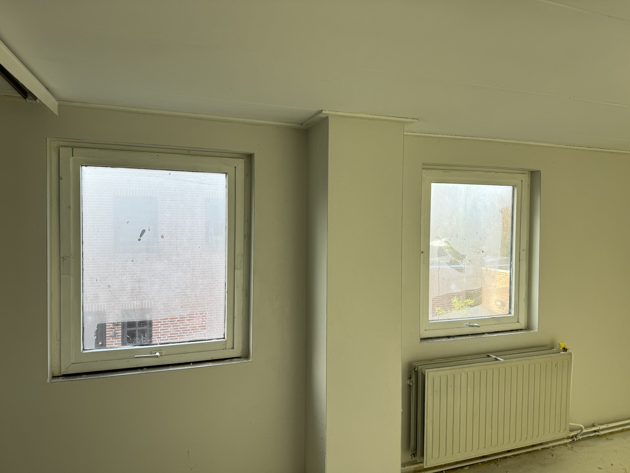 Kamer met vers gestucte wanden rond twee ramen en een radiator