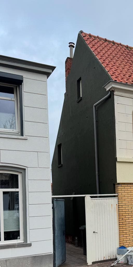 Hoge zijgevel afgewerkt in antraciet stucwerk naast een witte woning