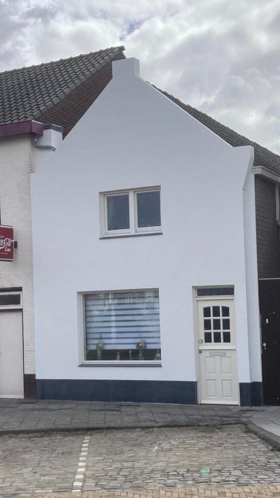 Kleine woning met puntgevel, strak wit gestuct met donkere plint